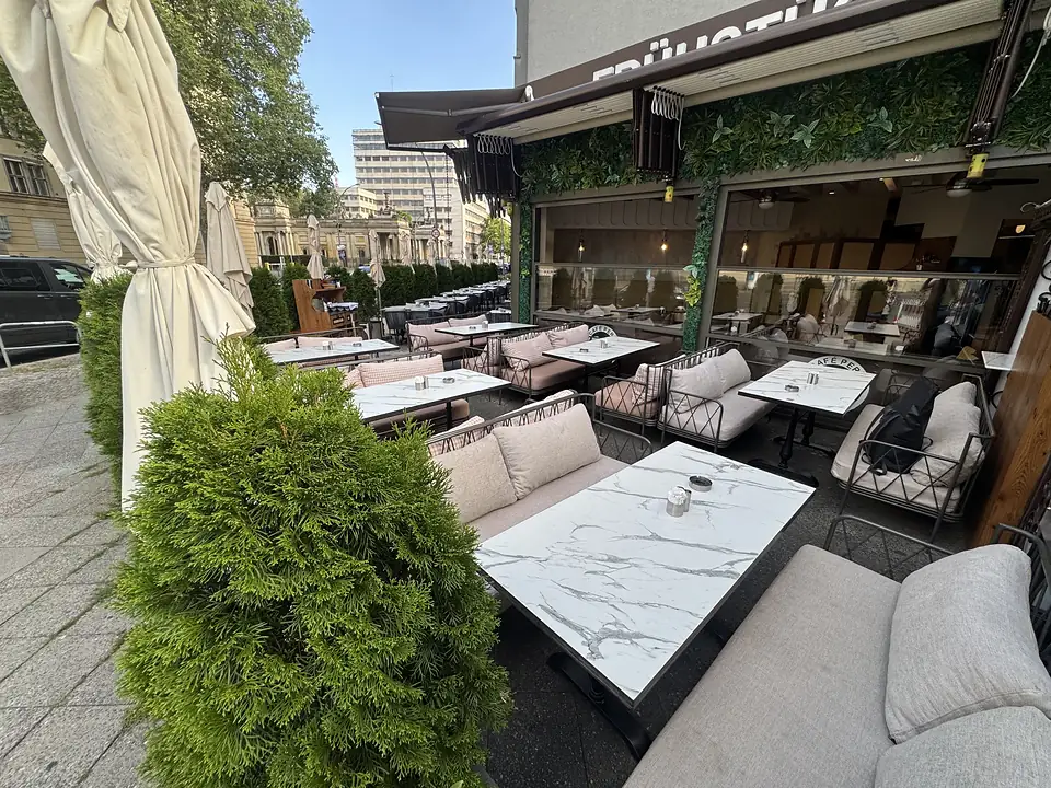 Sonnige Terrasse des Café Peri an der Potsdamer Straße in Berlin-Schöneberg mit gedeckten Tischen unter der Markise.